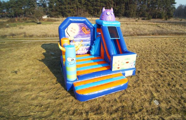 Bunte Hüpfburg mit Rutsche und Spielstationen auf einem grünen Feld.