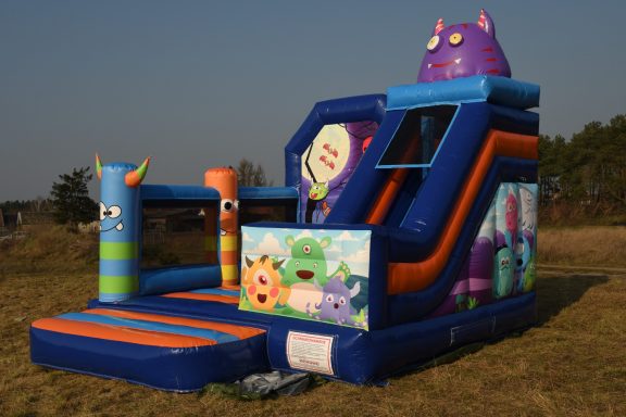 Bunte Hüpfburg mit Monster-Motiven und Rutsche in einem Feld.