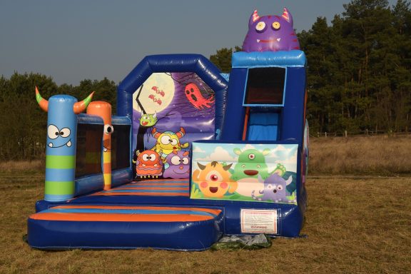 Bunte Hüpfburg mit Monster-Motiven, Kletterwand und rutschiger Fläche im Freien.